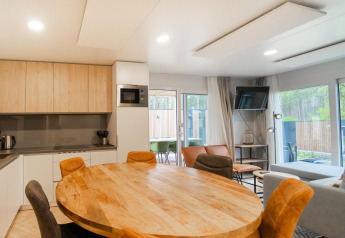 Moderna sala de estar y cocina en una cabaña Belsano en Hoge Kempen, Bélgica, con muebles de madera y ventanales.