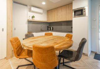 Modern kitchen and dining area at Belsano lodge in Hoge Kempen, Belgium, with a wooden round table and chairs.