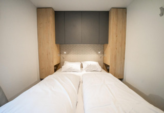 Cama moderna con sábanas blancas, armarios de madera y pared decorada en Belsano Lodge, Hoge Kempen, Bélgica.