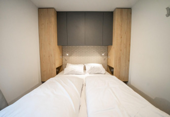 Modern bed met witte lakens, houten kasten en decoratieve muur bij Belsano Lodge in Hoge Kempen, België.