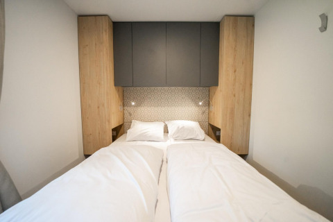 Cama moderna con sábanas blancas, armarios de madera y pared decorada en Belsano Lodge, Hoge Kempen, Bélgica.