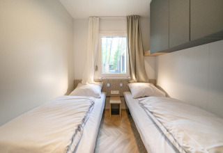 Habitación de lodge moderna con dos camas individuales, ventana y cortinas claras en Belsano, Hoge Kempen, Bélgica.