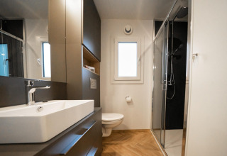 Baño moderno en la Belsano lodge de Hoge Kempen, Bélgica, con ducha acristalada y suelo de madera clara.
