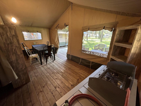Interior de una tienda glamping con suelo de madera, mesa de comedor, sillas, estufa de gas y estanterías