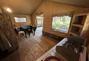 Interieur van een glamping-tent met houten vloer, eettafel, stoelen, gasfornuis, planken en tuinzicht