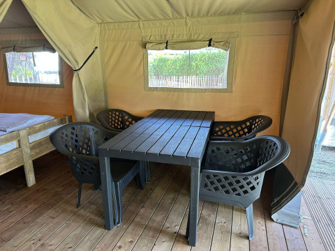 Interno di una tenda glamping con pavimento in legno, quattro sedie nere e tavolo vicino a un letto.
