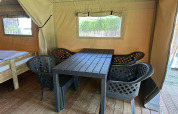 Intérieur d'une tente glamping avec plancher en bois, quatre chaises noires et une table près d'un lit.