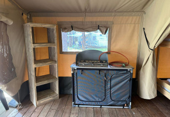 Intérieur d'une tente de glamping avec une cuisinière à gaz, une étagère en bois et un plancher en bois.