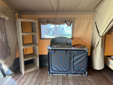 Interior de una tienda glamping con estufa de gas, estantería de madera y suelo de madera para mayor confort.