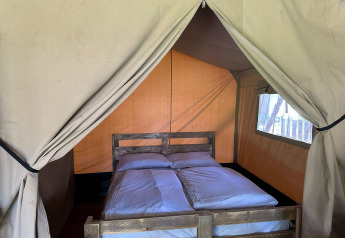 Intérieur d'une tente de glamping avec un lit double, une literie blanche et un cadre en bois, vue de face.