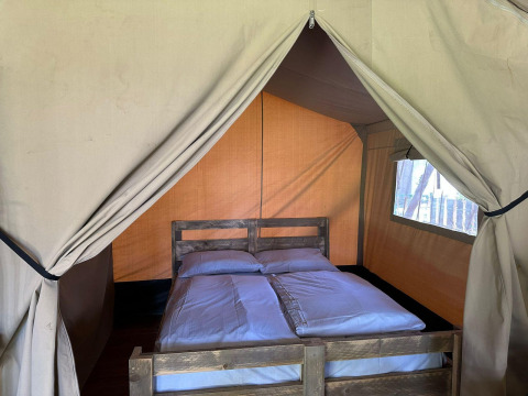 Indersiden af et glamping-telt med en dobbeltseng, hvidt sengetøj og trægulv, set forfra.