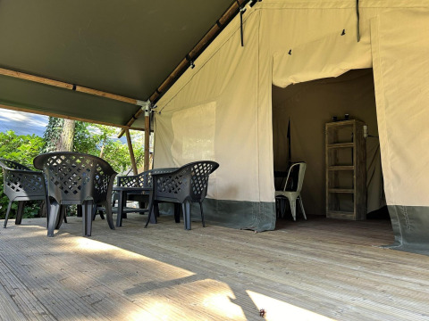 Terraza exterior en un alojamiento glamping con sillas de plástico, mesa y entrada de tienda al fondo.