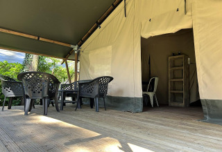 Udendørs terrasse ved glamping-indkvartering med plastikstole, bord og teltindgang i baggrunden.