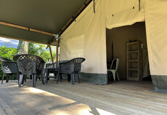 Terraza exterior en un alojamiento glamping con sillas de plástico, mesa y entrada de tienda al fondo.