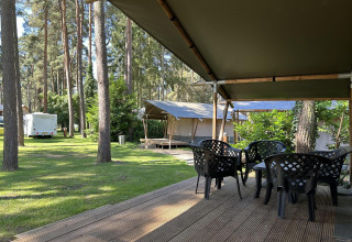 Vista da una terrazza coperta con sedie di plastica in un glamping circondato da alberi e tende.