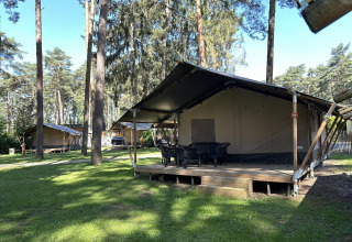 Un alojamiento glamping en el bosque con tiendas grandes sobre plataformas de madera, mesa y sillas.
