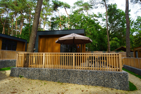 Buitenzicht op de Cube La Mer tiny house met houten terras, parasol en omgeven door weelderig bos.