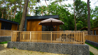 Buitenzicht op de Cube La Mer tiny house met houten terras, parasol en omgeven door weelderig bos.