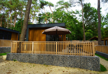 Vista exterior de la tiny house Cube La Mer con terraza de madera, sombrilla y rodeada de bosque.