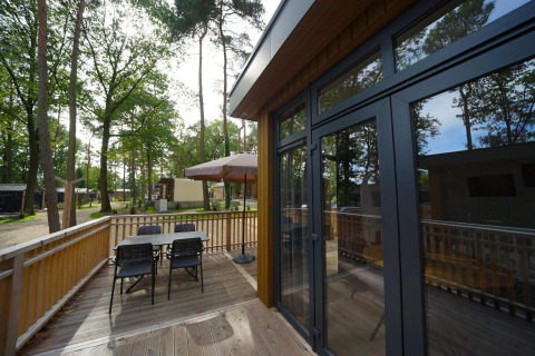 Buitenterras aan tiny house Cube La Mer in Hoge Kempen, België met tafel, stoelen en grote parasol.