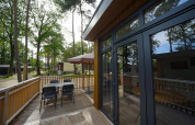 Buitenterras aan tiny house Cube La Mer in Hoge Kempen, België met tafel, stoelen en grote parasol.