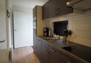 Cocina moderna en la tiny house Cube La Mer en Hoge Kempen, Bélgica, con gabinetes grises y electrodomésticos.