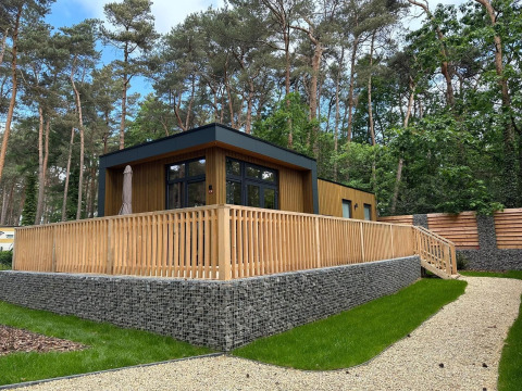 Moderne tiny house Cube La Mer in Hoge Kempen, België, met houten terras en omringd door bos.