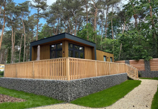 Moderne tiny house Cube La Mer in Hoge Kempen, België, met houten terras en omringd door bos.