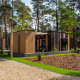 Moderne tiny houses kaldet Forest Cottage ligger i en frodig skov, omgivet af grønne træer og stier.