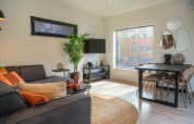Moderne lille stue i Forest Cottage ved Hoge Kempen, Belgien, med sofa, spisebord og store vinduer.