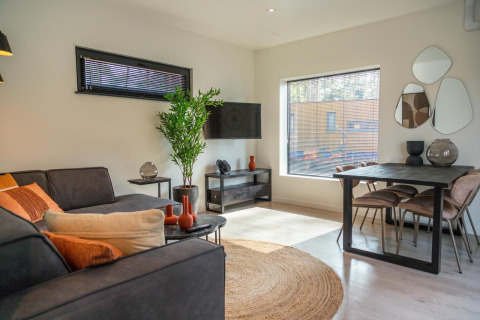 Modernes Wohnzimmer im Forest Cottage bei Hoge Kempen, Belgien, mit Sofa, Esstisch und großen Fenstern.