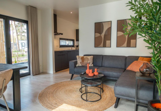 Modernes Wohnzimmer mit grauem Sofa, orangen Dekoren und Kunstwerken im Forest Cottage, Hoge Kempen, Belgien.