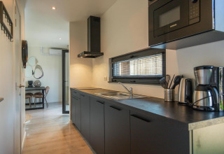 Cocina moderna en Forest Cottage, Hoge Kempen, Bélgica, con armarios negros y electrodomésticos de acero inoxidable.