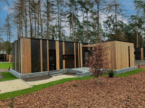 Modernes Tiny House namens Forest Cottage im Hoge Kempen, Belgien, mit Holz- und Steinoptik im Wald.