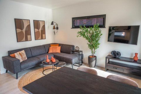 Sala moderna en Forest Cottage, Hoge Kempen, Bélgica, con sofá negro, arte abstracto y planta verde.