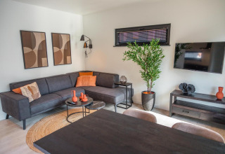 Sala moderna en Forest Cottage, Hoge Kempen, Bélgica, con sofá negro, arte abstracto y planta verde.