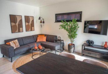 Stilfuld stue i Forest Cottage, Hoge Kempen, Belgien, med sort sofa, kunst og grøn plante.