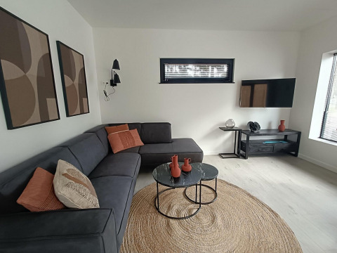 Sala moderna en Forest Cottage, Hoge Kempen, Bélgica, con sofá en esquina, mesas redondas y arte en la pared.