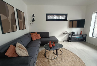 Sala moderna en Forest Cottage, Hoge Kempen, Bélgica, con sofá en esquina, mesas redondas y arte en la pared.