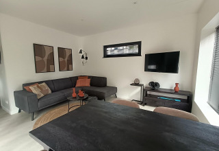 Sala moderna en la tiny house Forest Cottage en Hoge Kempen, Bélgica, con sofá esquinero y televisor.