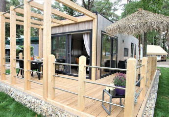 Kempen cottage lodge con terrazza in legno moderna, ampie vetrate e area salotto all'aperto nel verde.