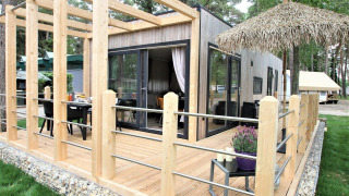 Kempen cottage lodge con terrazza in legno moderna, ampie vetrate e area salotto all'aperto nel verde.