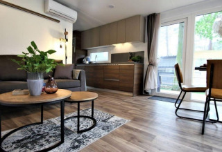 Sala y cocina modernas en la cabaña Kempen, Hoge Kempen, Bélgica, con muebles cálidos y ventanales.