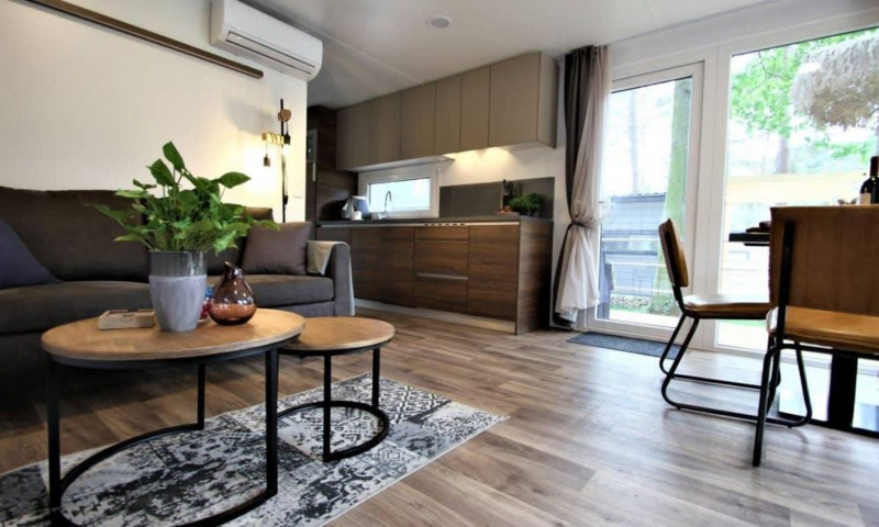 Sala y cocina modernas en la cabaña Kempen, Hoge Kempen, Bélgica, con muebles cálidos y ventanales.