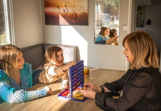 Tres personas juegan un juego de mesa en una mesa en Kempen cottage, Hoge Kempen, Bélgica, con luz solar.