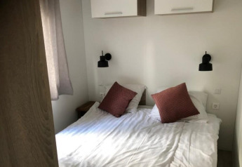 En dobbelt seng med hvide lagner og to brune puder i Kempen-hytten på Hoge Kempen, Belgien.