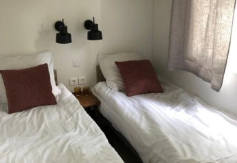 Zwei Einzelbetten mit weißen Bettbezügen und braunen Kissen im Kempen Cottage, Hoge Kempen, Belgien.