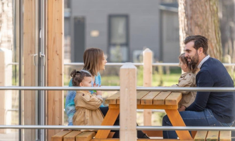 Familie sidder ved et piknikbord udenfor Kempen cottage på Hoge Kempen i Belgien og nyder tiden sammen.