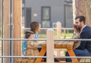 Familie sidder ved et piknikbord udenfor Kempen cottage på Hoge Kempen i Belgien og nyder tiden sammen.