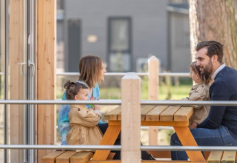 Familie sidder ved et piknikbord udenfor Kempen cottage på Hoge Kempen i Belgien og nyder tiden sammen.